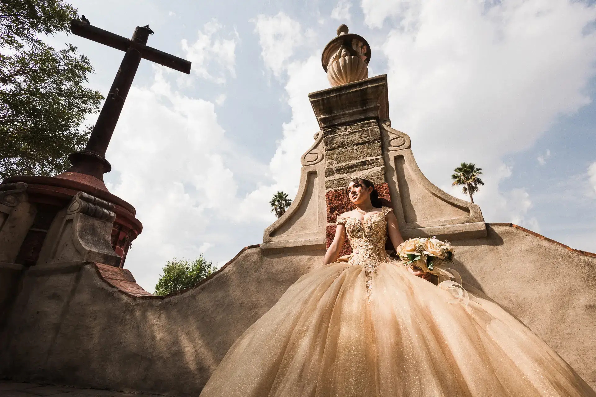 Quinceañera con vestido dorado bajo cruz colonial mexicana con cielo abierto, sesión XV años por Jorge Salgado