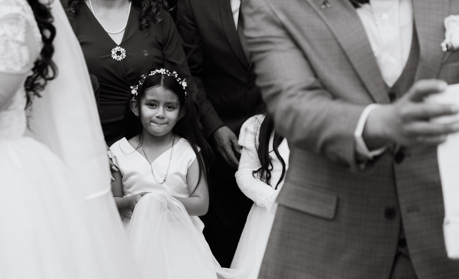 Niña con corona de flores entre los novios durante la ceremonia — momento documental en blanco y negro