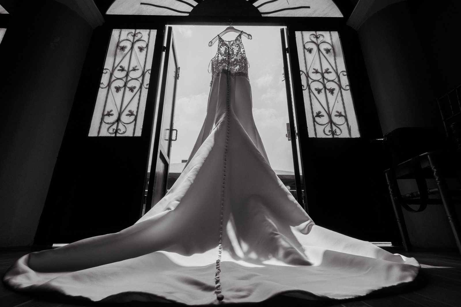 Vestido de novia colgado en puerta a contraluz — detalle editorial en blanco y negro