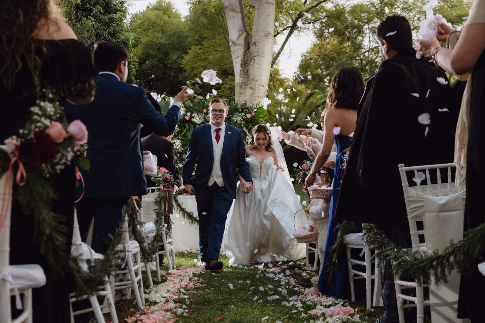 Novios saliendo de la ceremonia entre invitados que arrojan pétalos de rosa