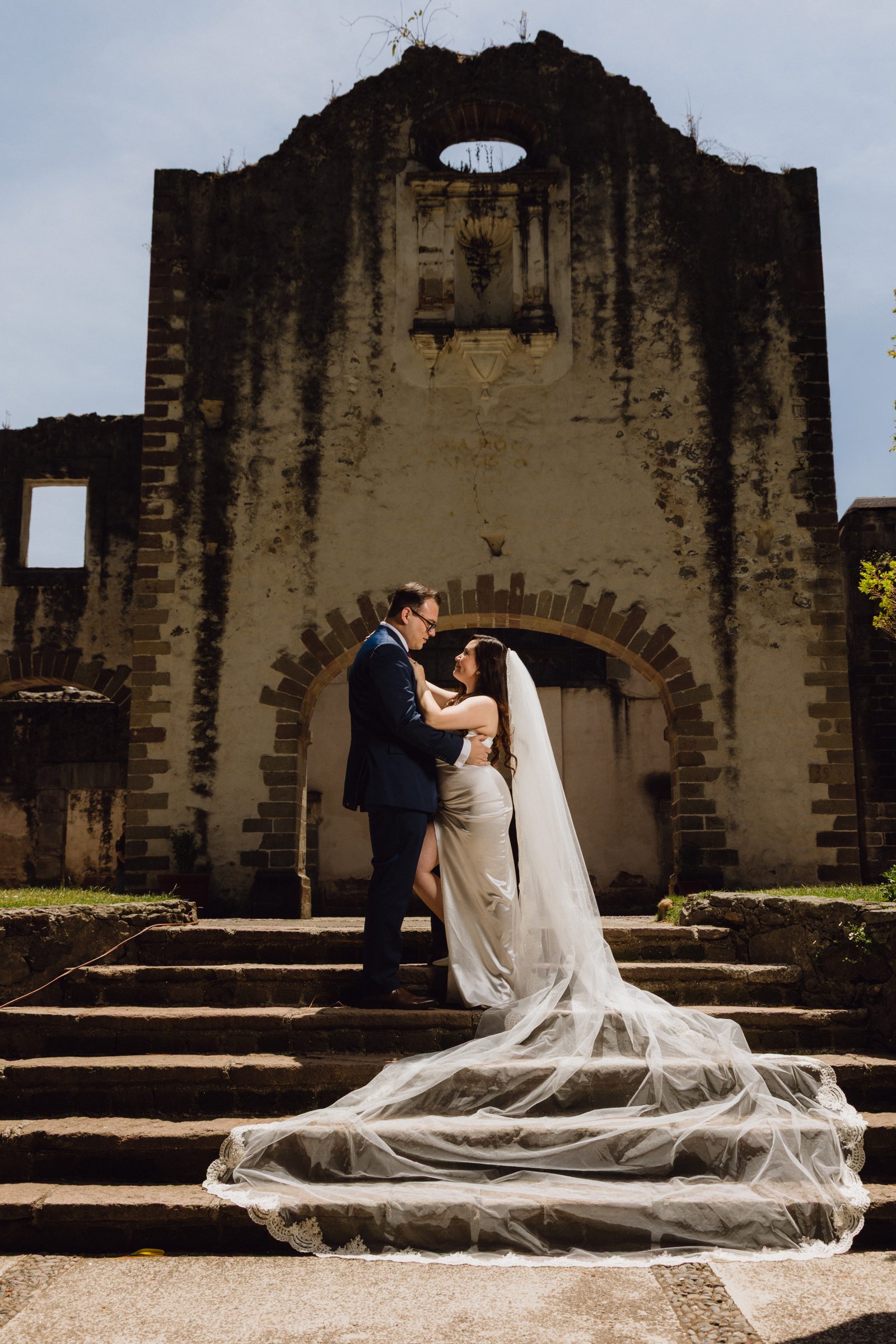 Novios en bosque con novia vestida de blanco con botas vaqueras y novio con sombrero — estilo campestre mexicano