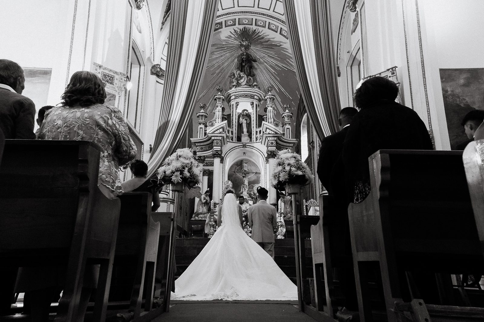 Novios frente al altar barroco de iglesia colonial mexicana durante la ceremonia religiosa, fotografía documental de boda en blanco y negro — Salicatus