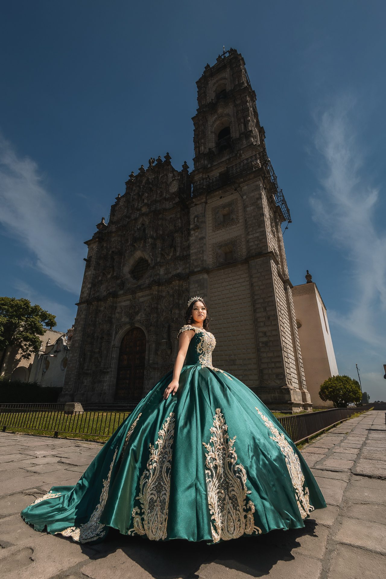 Quinceañera con vestido verde esmeralda y bordados dorados frente a iglesia barroca de Tepotzotlán, sesión de XV años editorial — Salicatus